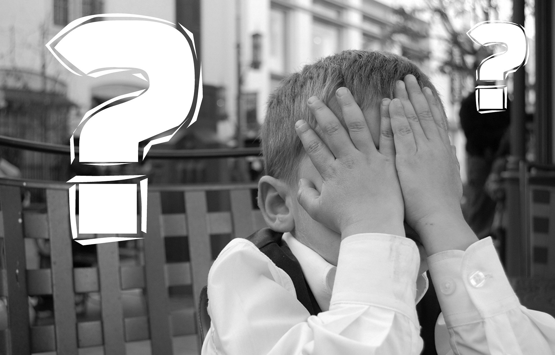 Young boy covering his head with question marks around him